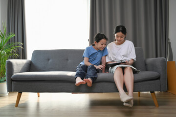 Two young asian girl watching funny video on digital tablet while sitting on sofa.