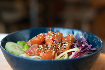 wok in a blue plate on a wooden table with peas, fish, sesame seeds and cucumber, healthy lunch