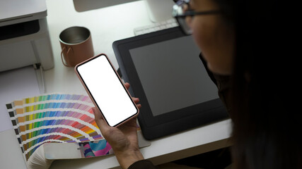 Close up view of creative woman sitting at her workplace and using smart phone for texting or massaging with her friends.