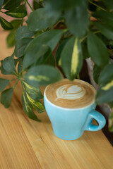 
coffee with foam and a pattern in a blue mug on a wooden table near a green plant
