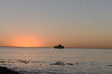 Scenic seascape as the sun sets beautifully with a cargo ship in the far horizon.