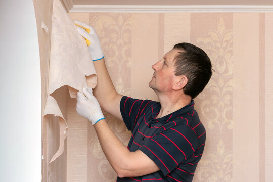 Man, repairman removes old wallpaper from the wall, replacing wallpaper