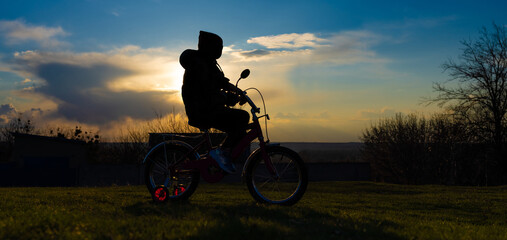 Obraz premium A seven-year-old girl learning to ride a tricycle at sunset in the spring