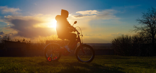 A seven-year-old girl learning to ride a tricycle at sunset in the spring