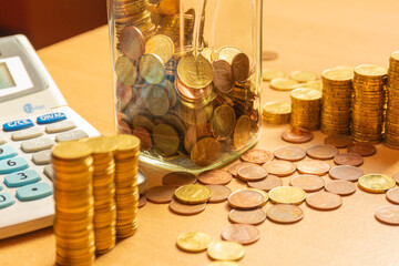 Pile of coins on a table with a lot of different coins around it and a calculator on a wooden table. Save money concept banner.