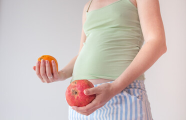 Pregnant girl with fruits. The concept of bearing healthy offspring, replenishing vitamin deficiencies during pregnancy and lactation. Pregnant belly and orange with pomegranate in hands