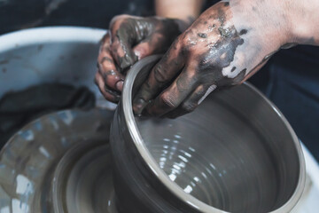 Working with a potter's wheel with gray clay. The hands of a girl potter.