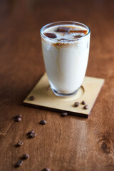 Ice coffee in a tall glass with cream poured over and coffee beans. Cold summer drink on a cafe table