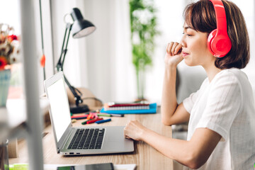 Young smiling asian woman relaxing using laptop computer and drinking coffee in bedroom at home.Young creative girl working and video conference online meeting with colleagues.work from home concept