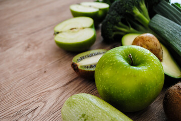 Green vegetables and fruits on a wooden background.