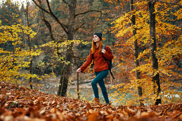 woman tourist walks through the park in autumn with a backpack on her back and tall trees landscape river lake