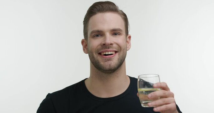 Smiling Man Drinking Water From Glass Showing Cool Looking At The Camera. Wearing Black T - Shirt Isolated On White Background. Attractive Guy Care Of Health. Wellness Concept. Daily Routine.