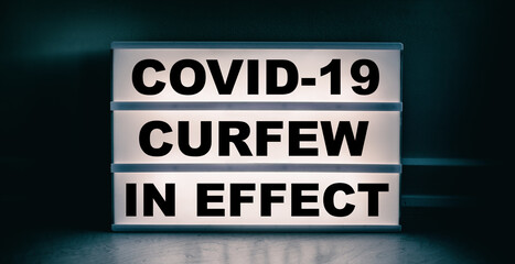 Fototapeta premium Curfew in effect text message on lit lightbox for covid coronavirus pandemic. Warning at night.