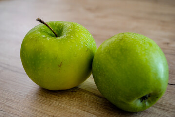 Two fresh green apples on a wooden background.