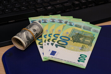 One hundred euro bills and a roll of one hundred dollar fanned out on a computer keyboard.