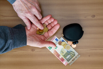 Hands counting small coins. There is a wallet and a euro on the table.
