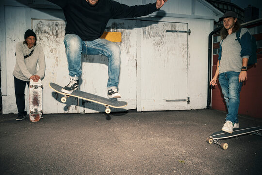 Male skater with skateboard jumping by friends on street