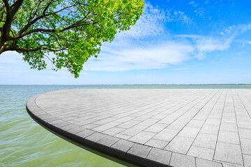 Empty square floor and green tree with lake landscape under the blue sky.