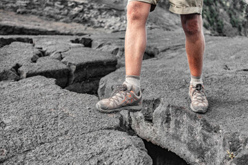 Hiking shoes man hiker on Hawaii island lava rock hike climbing over big open crack in ground....