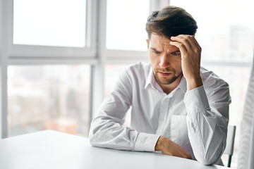 puzzled man sitting at a table indoors and touching his head with his hand