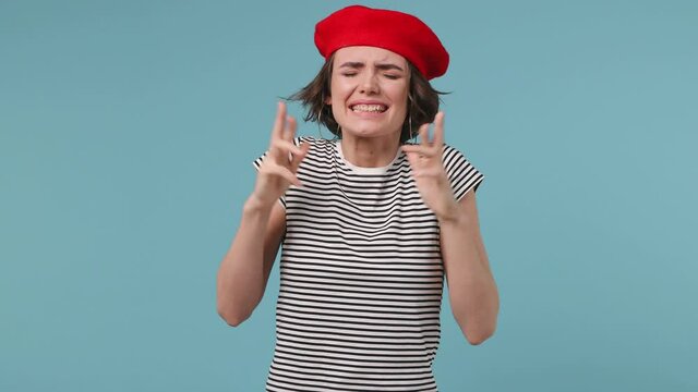 Pleading young woman 20s wear red french beret hat striped t-shirt hold hands folded in prayer begging about something making wish keep fingers crossed isolated on pastel blue color background studio