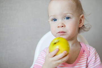 A little girl tastes, examines and plays with fresh apples with pleasure and interest. High quality photo