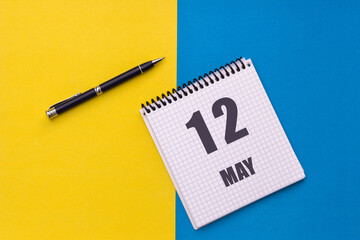 May 12th. Day 12 of month, calendar date. Notebook with a spiral and pen lies on a yellow-blue background