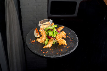 Tempura shrimps with fresh herbs and sauce on a black plate