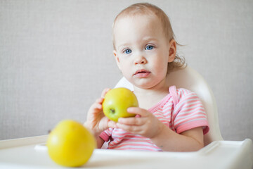 A little girl tastes, examines and plays with fresh apples with pleasure and interest. High quality photo