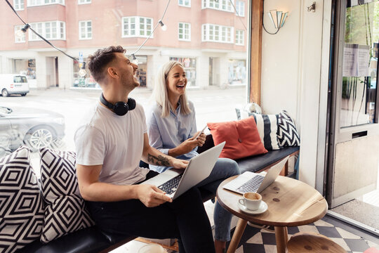 Male and female freelancer laughing while working on laptop at cafe