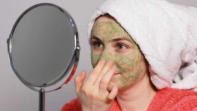A young woman in a pink bathrobe applies an Ayurvedic blend of ubtan to her face. Facial skin toning, scrubbing, prevention of wrinkles and blackheads in women