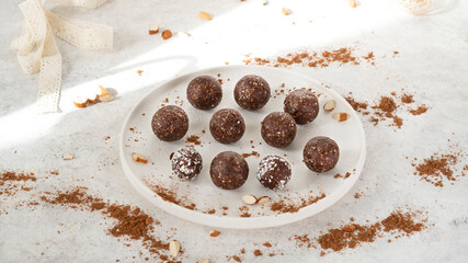Homemade healthy raw vegetarian dessert energy balls with nuts, dates, peanut butter, cocoa powder, coconut flakes and oats on white plate with sunlight. Healthy eating. Fitness snack. Selective focus