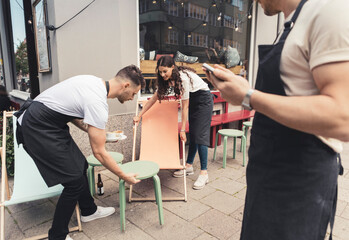 Male and female entrepreneurs arranging tables and chairs outside cafe