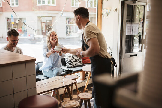 Smiling owner giving coffee to female customer at cafe - Powered by Adobe