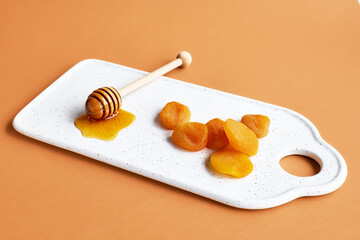 Dried apricots and honey in white plate on orange background. Dehydrated fruits. Healthy sweets concept.