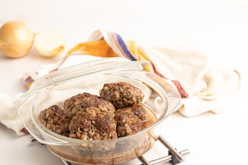 Cooked homemade fresh fried meatballs made from beef and pork meat in a glass saucepan stands on the table.