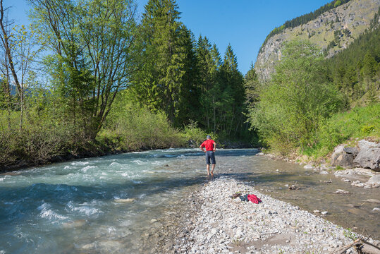 man at the riverbed with bare foots, hardening in the cold river at springtime