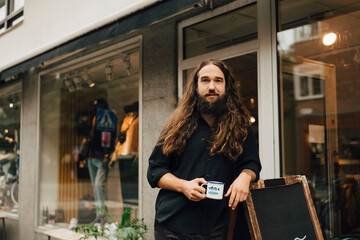Male entrepreneur with coffee cup standing outside retail store