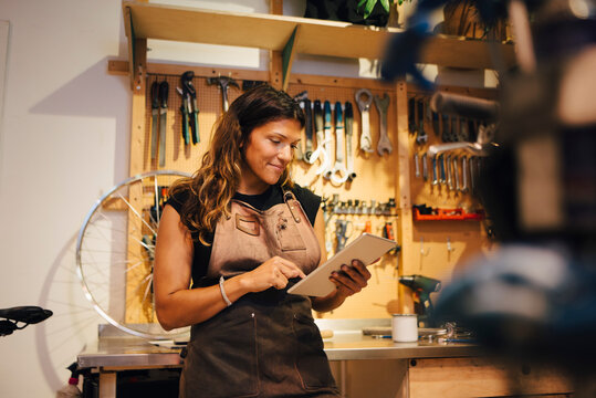Smiling female owner using digital tablet at bicycle workshop - Powered by Adobe