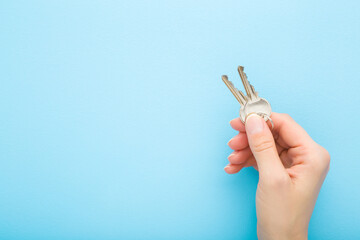 Young adult woman hand holding two metal door keys on light blue table background. Pastel color....