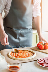chef smears tomato sauce on the pizza dough
