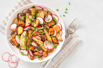 Vegan salad of baked vegetables, radishes and herbs in a plate on a white background. Copy space for text. Salad of potatoes, carrots, Brussels sprouts and fresh radishes. Vegetarian food.
