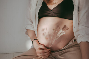 Pregnant belly close up in neutral tones and dried flowers in wabi sabi style. Pregnant woman and...
