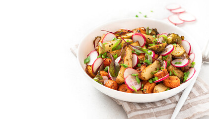 Vegan salad of baked vegetables, radishes and herbs in a plate on a white background. Copy space for text. Salad of potatoes, carrots, Brussels sprouts and fresh radishes. Vegetarian food.