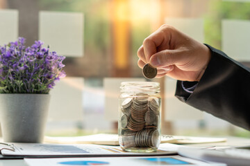 businessman saving money concept. hand holding coins putting in jug glass