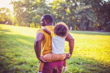 Father carrying daughter piggyback. African American father and daughter having fun outdoors.