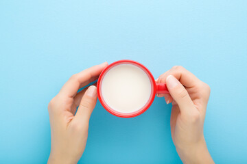 Young adult woman hands holding red mug of white fresh milk on light blue table background. Pastel color. Closeup. Point of view shot. Healthy drink concept. Top down view.