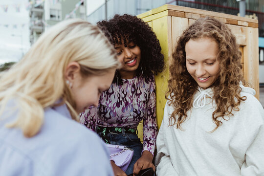 Smiling female friends looking down by box container outdoors