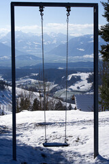 Swing in the backlight with beautiful panoramic landscape with snow capped Swiss alps in the background. Photo taken April 8th, 2021, Bachtel, Switzerland.