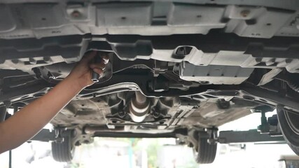 Mid adult mechanic repairing undercarriage of a car in auto repair shop.